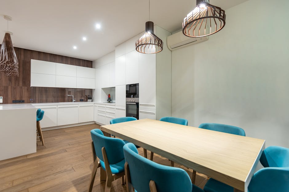 Set of turquoise chairs at table placed in stylish spacious kitchen with white cupboards and modern light kitchenware at home