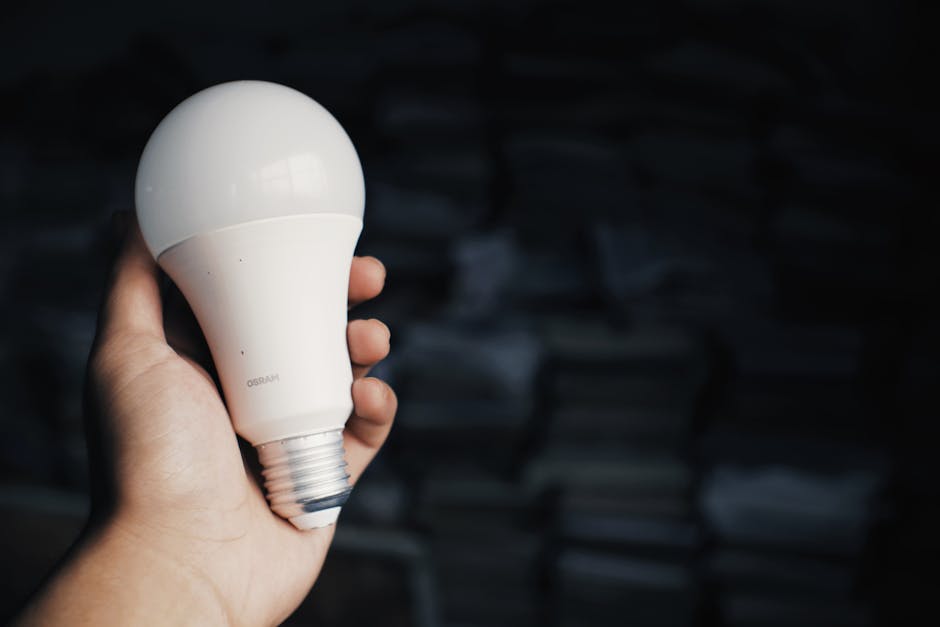 Crop anonymous person showing light bulb in hand against heap of books in dark room