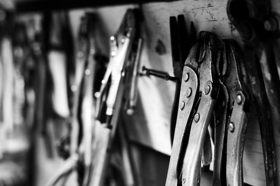 A monochrome close-up of locking pliers and tools hanging in a workshop.