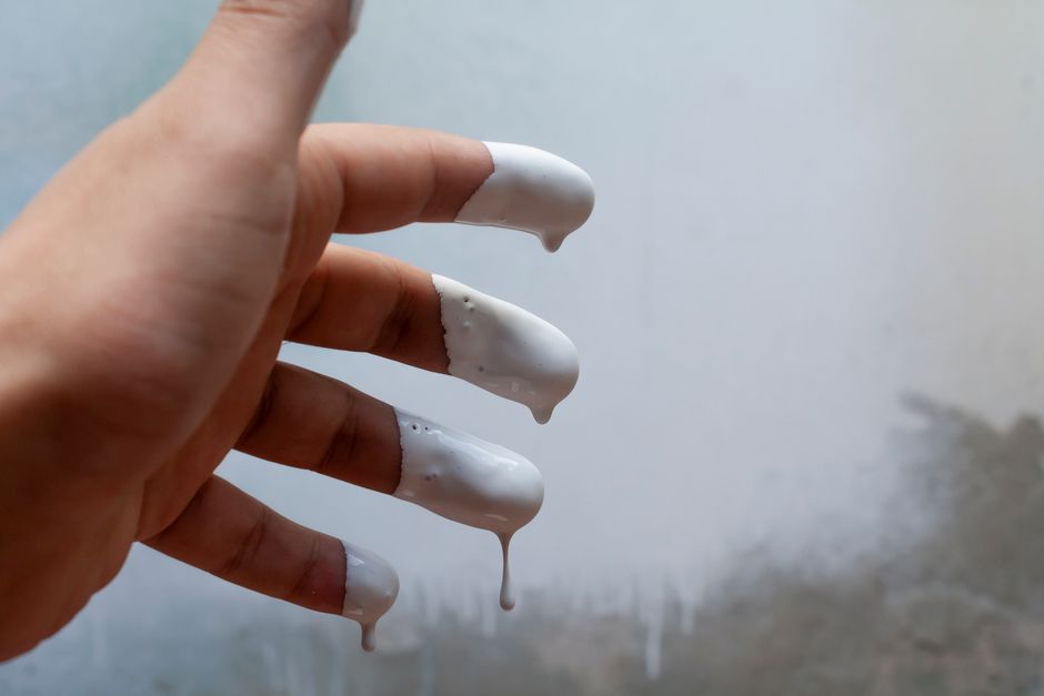 Close-up of fingers covered in dripping white paint, showcasing artistic creativity.