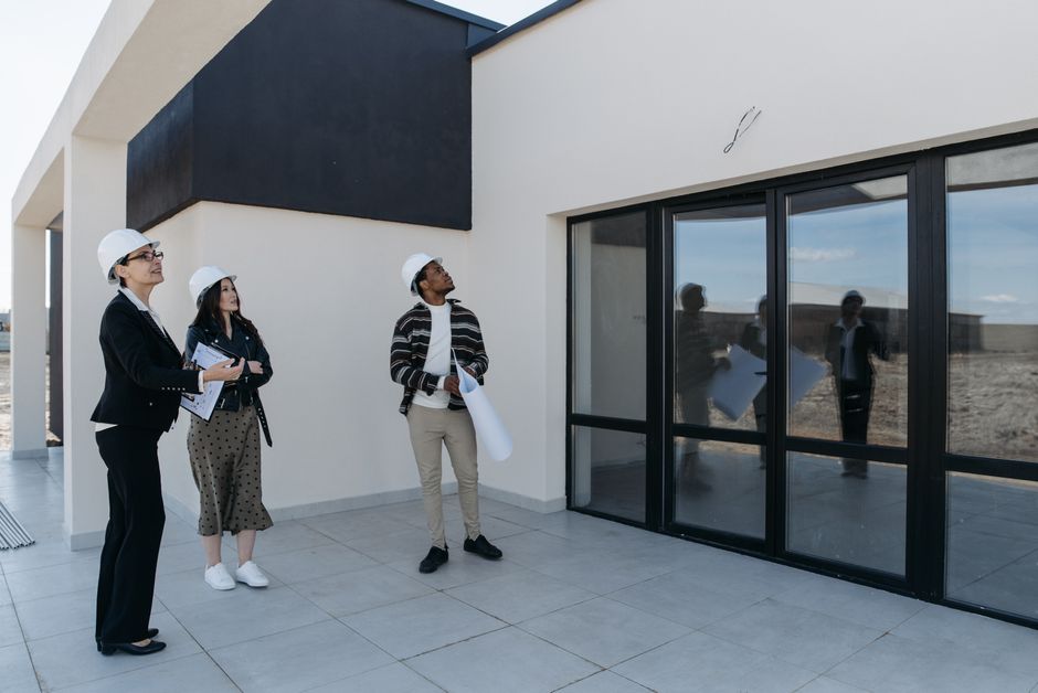 Architects in hard hats discuss the structure of a new building with large glass doors, suggesting a modern architectural design.