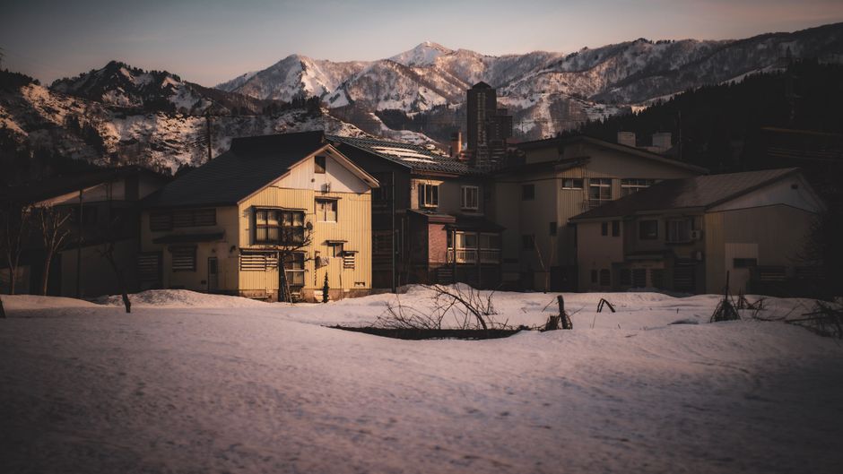 Charming village in Japan with snow-covered landscape and mountain backdrop during twilight.